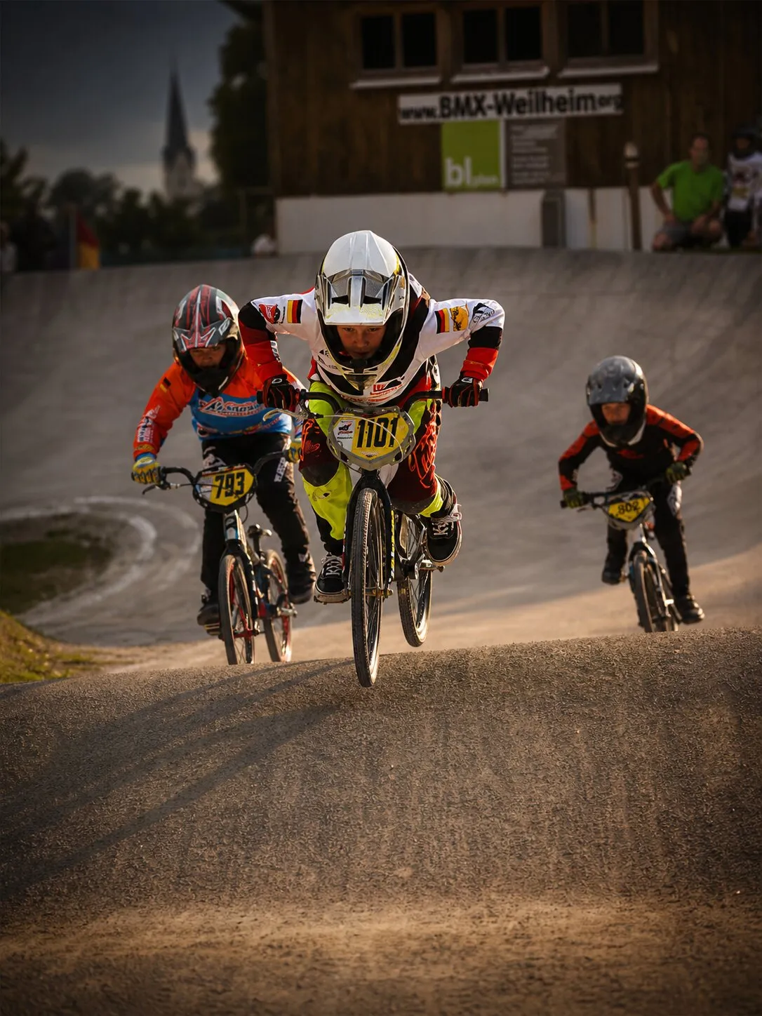 Drei junge BMX-Fahrerinnen und -Fahrer in Aktion auf der Strecke